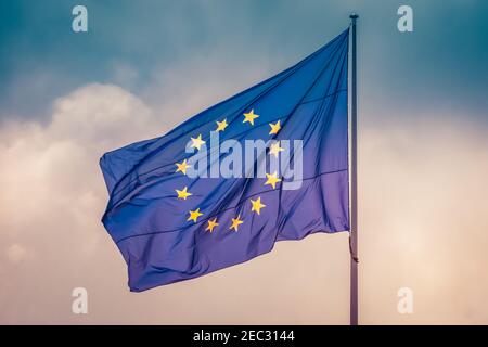 European Union flag waving in wind in colorful sky slightly cloudy. The official symbol of the EU. Stock Photo
