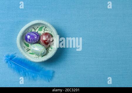 Traditional wooden painted Easter eggs with ornament on painted plate, blue feather and blue material background for copy space Stock Photo