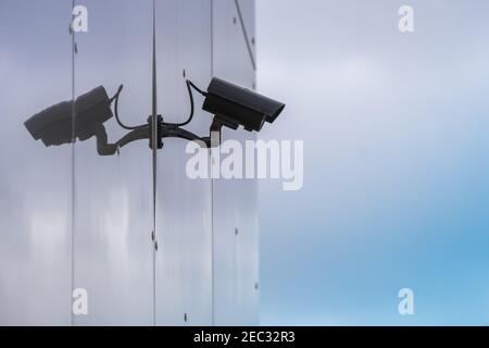 Modern CCTV security camera installed on building wall with reflection. Concept of surveillance and monitoring in city. Stock Photo