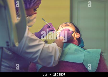 Male dentists examining and working on young female patient.Dentist's office. Real woman in a chair at the dentist. toned Stock Photo