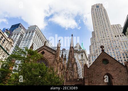View of the top part of Trinity Church in Financial District in New York with buildings in the background and cloudy blue sky Stock Photo