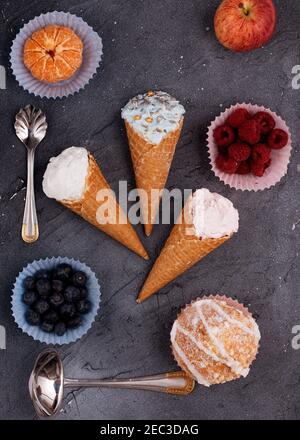 three ice cream, raspberry, blueberry, muffin, apple, and tangerine on grey background. View from above. Stock Photo