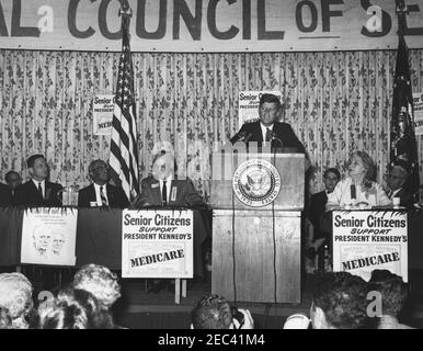 Address to the National Convention of the National Council of Senior Citizens, 11:47AM. President John F. Kennedy (at lectern) delivers an address to attendees of the National Convention of the National Council of Senior Citizens at the Willard Hotel, Washington D.C. On stage (L-R): unidentified (in back); Senator Birch Evans Bayh, Jr. of Indiana; Director of Special Projects for the Council, Lawrence A. Oxley; Council Chairman, John Fitzpatrick; President Kennedy; Executive Director of the Council, Dr. Blue Carstenson (in back); two unidentified. Stock Photo