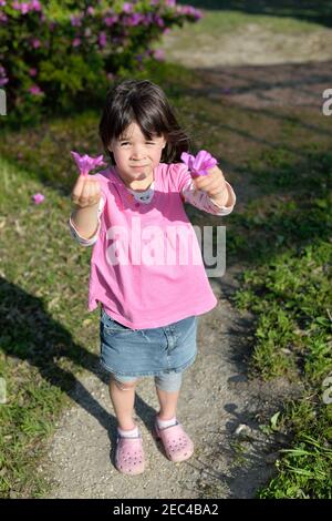 Little girl dressed in pink with a plaster on her knee holding pink flowers. Springtime. Stock Photo