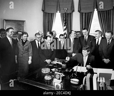 Bill signing - H.R. 7500 Public Law 87-293, Peace Corps Act, 9:45AM. President John F. Kennedy (laughing) signs HR 7500, the Peace Corps Bill, in the Oval Office, White House, Washington, D.C. Looking on (L-R): Senator Claiborne Pell of Rhode Island (in back); Director of the Peace Corps, R. Sargent Shriver; Senator Philip A. Hart of Michigan (in back); Representative Edna Kelly of New York; Representative Chester Merrow of New Hampshire; Representative Thomas F. Johnson of Maryland (in back); Representative Clement Zablocki of Wisconsin; Representative Wayne L. Hays of Ohio (partially hidden Stock Photo