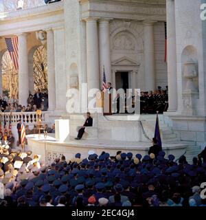Address at Veterans Day Ceremonies, Arlington National Cemetery, 11:01AM. President John F. Kennedy delivers remarks as part of Veterans Day ceremonies at Arlington National Cemetery in Arlington, Virginia. Persons sitting on the stage behind President Kennedy include: Thomas Stirling, National Commander of the Legion of Valor; Secretary of Defense Robert S. McNamara; Representative Olin E. Teague (Texas); Military Aide to the President General Chester V. Clifton; George W. Ball, Under Secretary for Economic Affairs; General Thomas D. White; Secretary of the Air Force Eugene M. Zuckert; Chairm Stock Photo