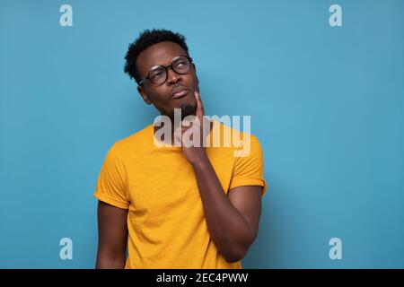 Young african man in glasses thinking over blue background. Studio shot Stock Photo