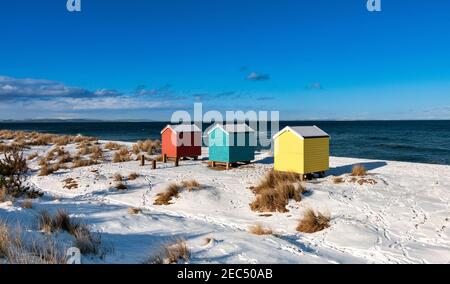 FINDHORN BAY MORAY FIRTH SCOTLAND THREE COLOURFUL HUTS OR CHALETS  ON A SNOW COVERED BEACH IN WINTER Stock Photo