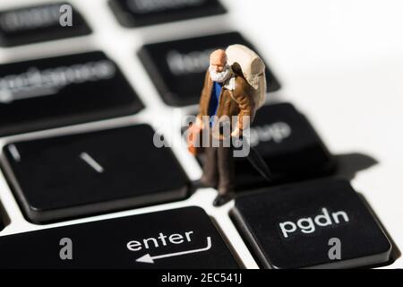 Tiny old traveler on white notebook keyboard with black buttons. Internet browsing or programming. Elder man computer education concept. Notebook keyb Stock Photo