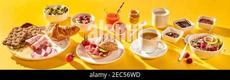 Breakfast panorama banner for advertising or menu on yellow with a wholesome spread of cereal, muesli, rolls, croissant, cold meat, cheese, olives, pr Stock Photo