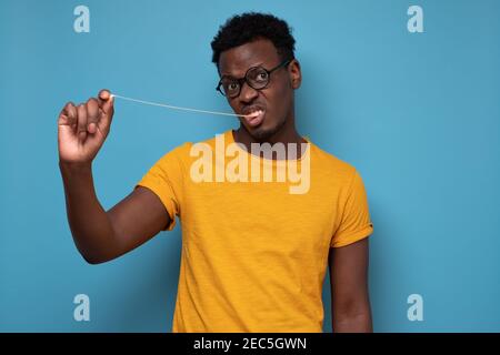 Young african man pulling a chewing gum. Studio shot on blue wall. Stock Photo