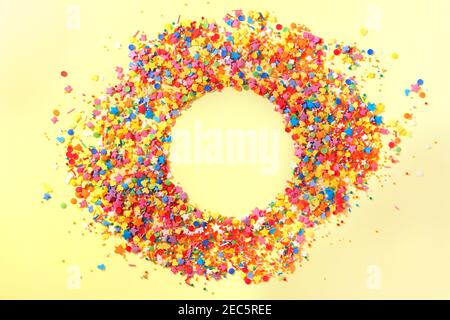 Sweet candy confetti in the middle of a circle with empty space for text. Yellow background Stock Photo