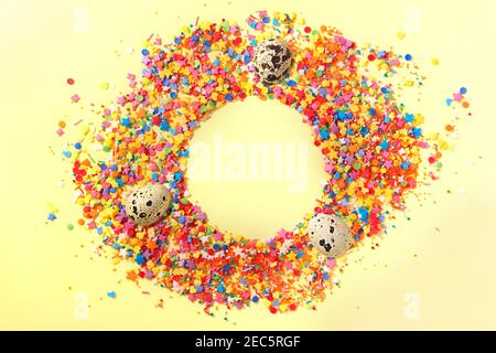 Sweet candy confetti in the middle of a circle with empty space for text and three quail eggs. Yellow background Stock Photo