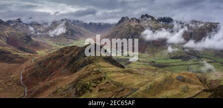 Epic flying drone landscape image of Langdale pikes and valley in Winter with low level clouds and mist swirling around Stock Photo