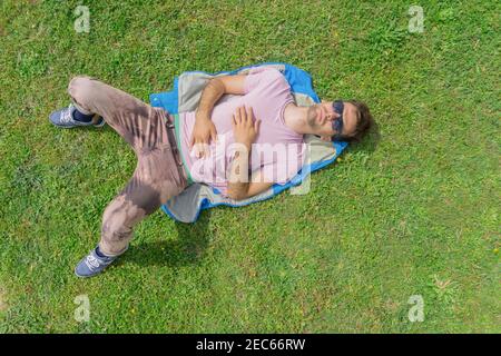 Handsome man lying on green grass, relaxing in hot summer day. Top view areal with copy space. Stock Photo
