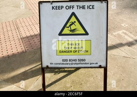 A 'Keep off thin ice'  sign warning 'Danger of Death' placed next to Whitestone Pond frozen over during Storm Darcy in Hampstead, London. Stock Photo