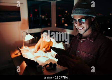 Caucasian male freelancer scrolling on digital tablet smiling receiving emails working late at night Stock Photo