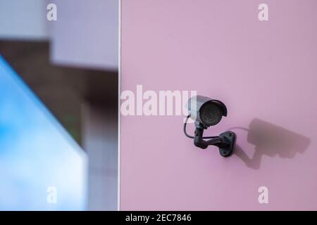 CCTV security camera on pink wall in modern city. Security system and monitoring concept. Copy space. Stock Photo