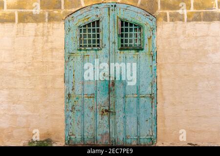 Vintage old warehouse blue wooden door with ancient brick wall of limestone. Front view of gates to abandoned warehouse in Malta Stock Photo