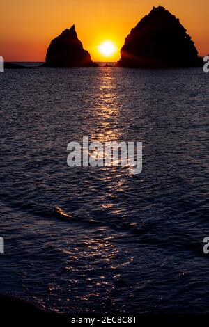 Sunset viewing the silhouettes of two huge rocks in the sea, with the setting sun between them. Near Myrina town, in Lemnos island, Aegean Sea, Greece Stock Photo