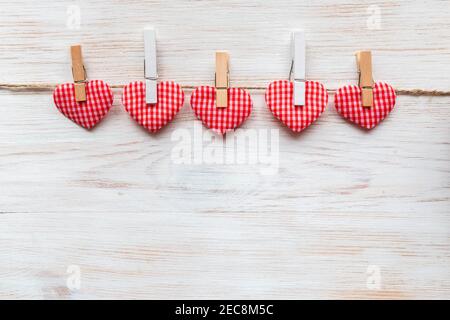 Sewed pillow red checkered hearts row border on clothespins at rustic white painted wood planks. Valentine's background. Happy lover's day concept. Co Stock Photo