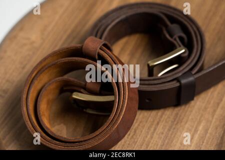 Two brown leather men's belts with bronze clasp on wooden chair with a white background. Handmade leather belt. Stock Photo