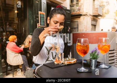 young woman eating italian bruschetta with stringy mozzarella cheese doing italian happy hour with spritz drink known as aperitivo in bar terrace Stock Photo