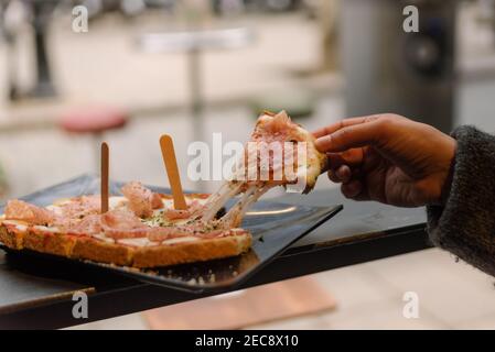 stringy mozzarella cheese bruschetta slice lifted by hand of woman eating bruschetta doing italian happy hour known as aperitivo in bar terrace. itali Stock Photo