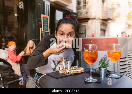 young woman eating bruschetta doing italian happy hour known as aperitivo in bar outdoor terrace. smiling and enjoying italian food and spritz Stock Photo