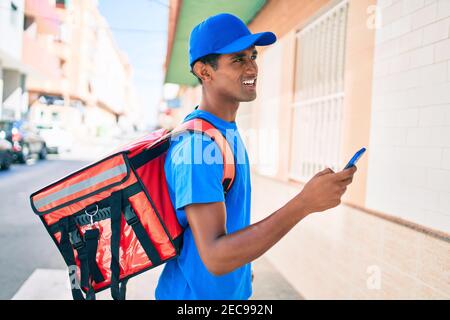 African delivery man wearing courier uniform outdoors using smartphone Stock Photo