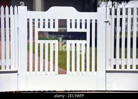 Cross is centered in the gate of a white, wooden picket fence.  Gate is closed. Stock Photo