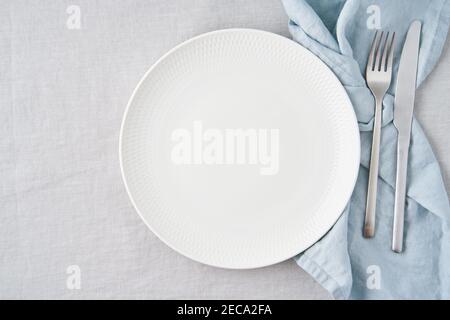 Clean empty white plate, fork and knife on pastel grey linen tablecloth on table, copy space Stock Photo
