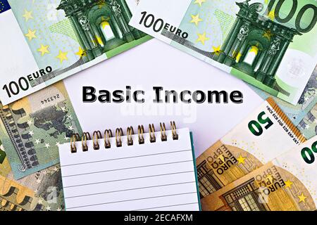 Topview photo on Universal Basic Income theme. The words Basic Income on paper, surrounded by banknotes Stock Photo