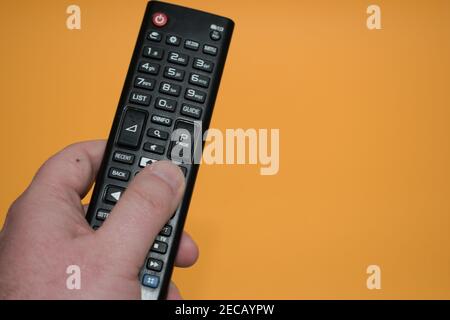 Hand holding black multimedia tv remote control on yellow background.Pushing button to change tv channel. Stock Photo