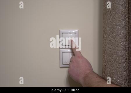Finger pressing light switch to turn off the light. Modern white light switch on white wall Stock Photo