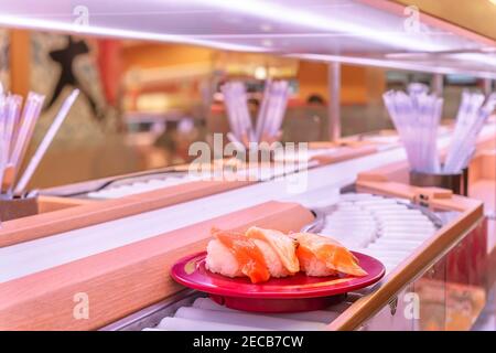Close up on the a conveyor belt sushi or Kaiten-zushi restaurant with a plate carrying three pieces of salmon sushi Photo -