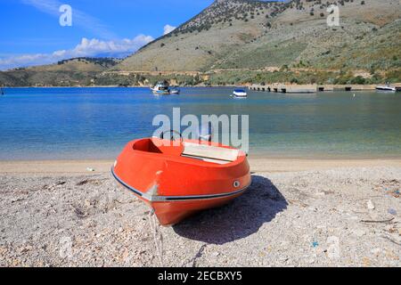 Red boat on the beach in the harbor in Porto Palermo, Albania Stock Photo