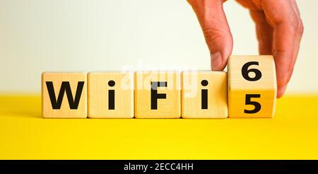 WiFi 5 or 6 symbol. Businessman turns a wooden cube and changes the words WiFi 5 to WiFi 6. Beautiful yellow, white background, copy space. Business, Stock Photo