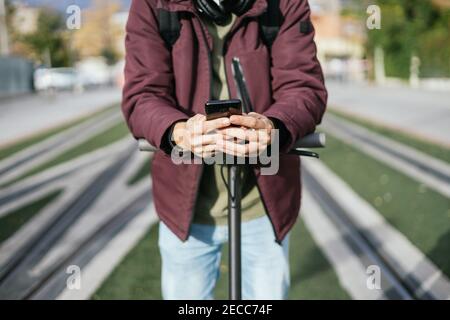 Hands of a student sending a message with his cell phone on the electric scooter. Stock Photo