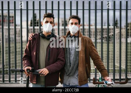 Two gay guys holding hands with a bicycle and an electric scooter looking at the camera. Stock Photo