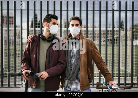 Two gay guys holding hands with a bicycle and an electric scooter looking at each other. Stock Photo