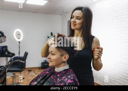 a girl hairdresser makes a hairstyle for a woman client in a modern beauty salon. Stock Photo