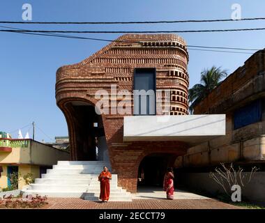 Exterior facade - late afternoon view with proud looking priest's wife and villager on phone. The Gallery House, Bansberia, India. Architect: Abin Des Stock Photo