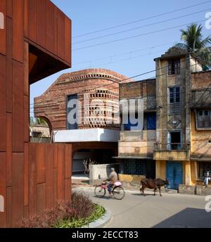 Street view with passing holy cow and villager on bike. The Gallery House, Bansberia, India. Architect: Abin Design Studio, 2020. Stock Photo