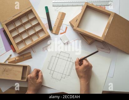 Designer draws a mockup for crafting cardboard box. Development of packaging design sketch. Stock Photo