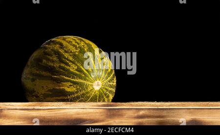 Green melon, for sale at farmers market, black background, on wood, with negative space. Stock Photo