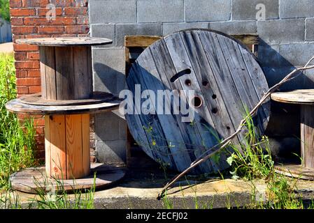 Empty, wooden cable spools are stacked against exterior wall of old building. Stock Photo