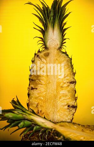 A fresh pineapple cut in half standing against a yellow background Stock Photo