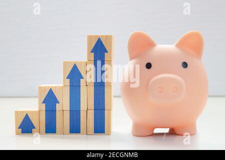 A piggy bank with wood blocks stacking as step stair with blue arrows up. Concept: Successful business, Business growth, Savings growth, Interest rate Stock Photo