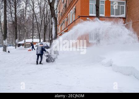A utility worker cleans a path with a snow blower during heavy snow on a winter day. A jet of snow takes off into the air. Stock Photo